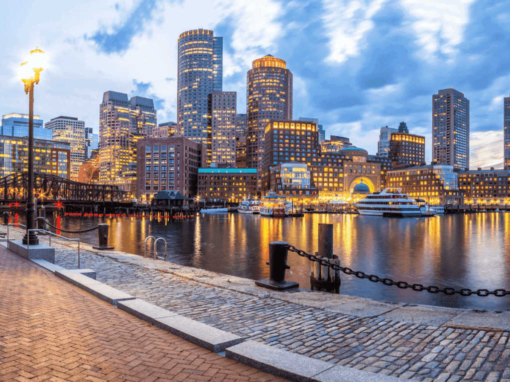 Landscape photo of Boston Harbor with water and boats in the foreground and skyscrapers in the background.